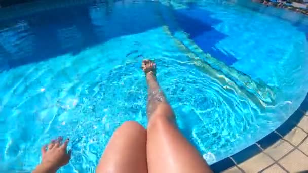 A woman is swinging her legs while sitting beside the swimming pool — Stock Video