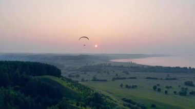 Gün batımında üzerlerinde uçan bir yelkenli ile yeşil ağaçlar. Gökyüzünde yamaç paraşütü.