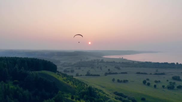 Alberi verdi al tramonto con una vela che vola sopra di loro. Parapendio nel cielo . — Video Stock