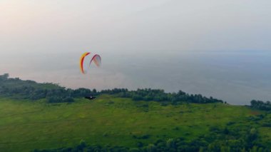 Yeşil ova ve üzerinde süzülen bir ram-hava paraşütü