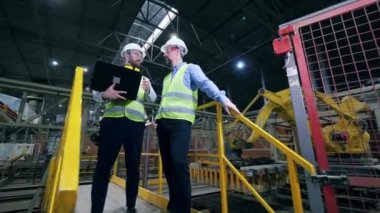 Erkek teknisyenler bir fabrika tesisinin ortasında duruyorlar..