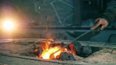 Demirci bir metal poker ile kömür taşır.