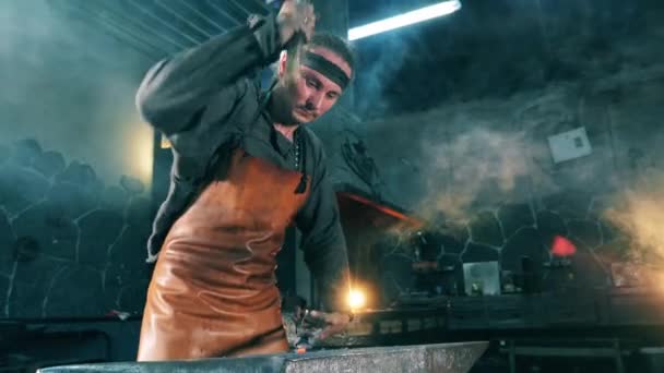 L'homme frappe un couteau en métal avec un marteau tout en travaillant à une forge . — Video