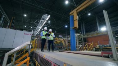 Erkek meslektaşları, endüstriyel uzmanlar modern fabrika tesisi boyunca yürüyorlar.
