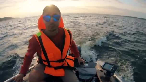 Een man in zonnebril en een leven vest is drijven in een boot — Stockvideo