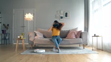 Bir kadın robotik elektrikli süpürgeyi kontrol ediyor, Vr gözlük takıyor.