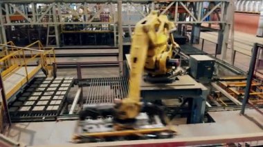 Fabrika zemininde robotik kol bir konveyör üzerinde tuğla sıralar.