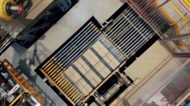 Büyük makine bir fabrika konveyörü üzerinde sarı tuğla taşır.