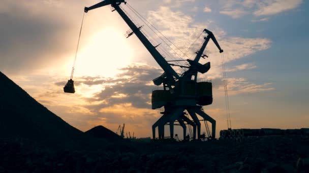 Grúas portuarias descargan escombros, trabajando sobre un fondo de puesta de sol . — Vídeos de Stock