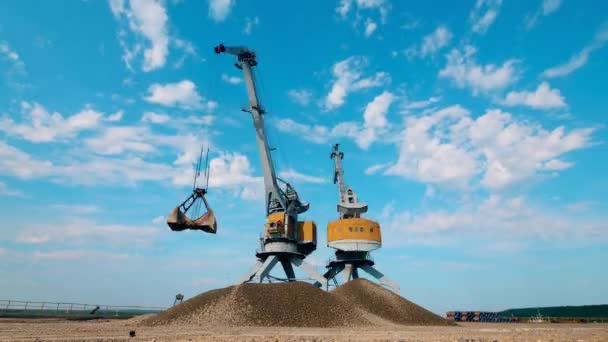 Twee havenkranen werken met verpletterde stenen en verplaatsen ze in stapels. — Stockvideo