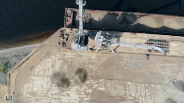 One crane carries crushed stones to stack them into a pile at port.
