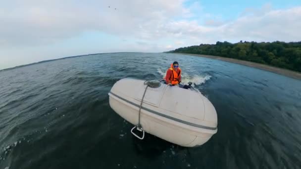 Молодий чоловік пливе на надувному човні з двигуном . — стокове відео