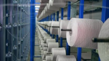 Tekstil fabrikası ekipmanları iş yerinde. Dikiş iplikli bobinler biriktirme sırasında metal bir rafa asılır.