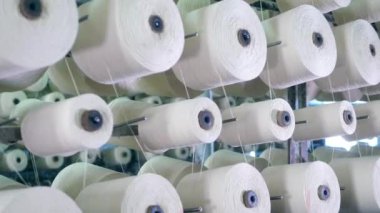 Tekstil fabrikası ekipmanları iş yerinde. Büyük bobinler iplikleri ile sarılmış, bir fabrika raf üzerinde dönen.