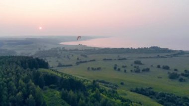 Tarlaların üzerinde bir yamaç paraşütünde uçan bir kişi.