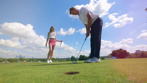 Игрок в гольф бросает мяч в лунку на поле для гольфа, пока женщина смотрит . — стоковое видео