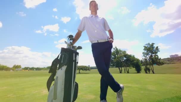 En golfare står på en bana med en påse med klubbor. — Stockvideo
