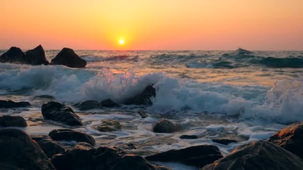 Olas golpeando contra rocas en una playa sobre un fondo de puesta de sol, cámara lenta . — Vídeo de stock