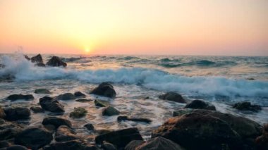 Gün batımı arka planında kıyı şeridine vuran beyaz dalgalar, yavaş çekim.