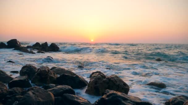 Olas marinas golpeando piedras en una playa sobre un fondo de puesta de sol, cámara lenta . — Vídeos de Stock