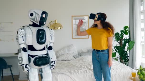 Uma senhora de óculos de realidade virtual está a tocar num robô parecido com um humano. Robô, humano como o conceito ciborgue . — Vídeo de Stock