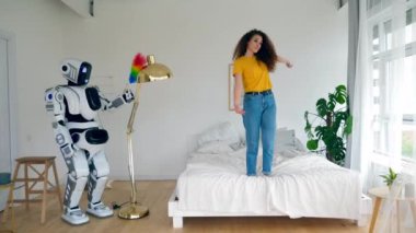Robot toz alıyor ve bayan yatakta dans ediyor. Akıllı ev konsepti.
