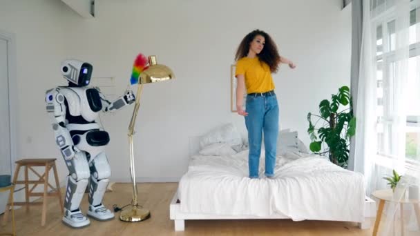 Robot sedang membersihkan debu dan wanita itu menari di tempat tidur. Konsep rumah cerdas . — Stok Video