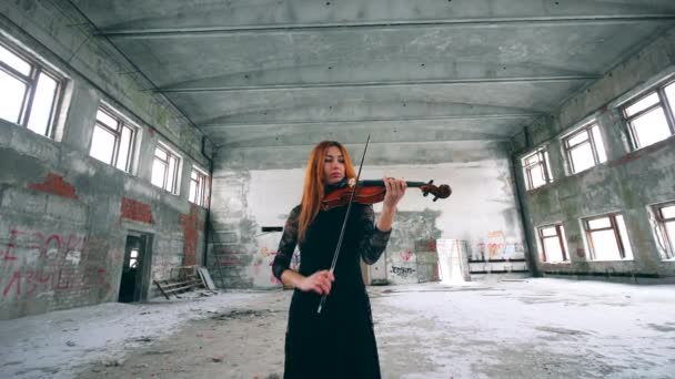 Рыжая леди играет на скрипке в заброшенном здании — стоковое видео