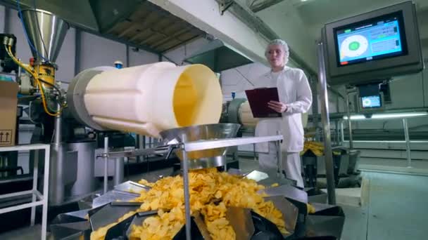 Vrouwelijke werknemer horloges een fabriek lijn vervoeren van gele chips. — Stockvideo