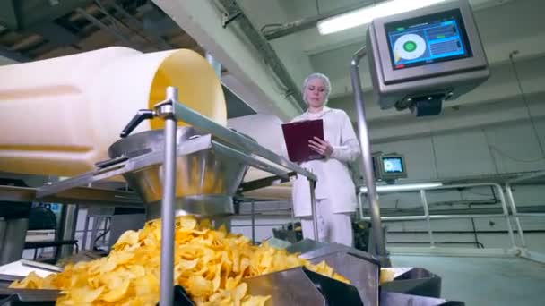 Kartoffelchips fallen in einen Container, während ein Fabrikarbeiter einen Prozess kontrolliert. — Stockvideo