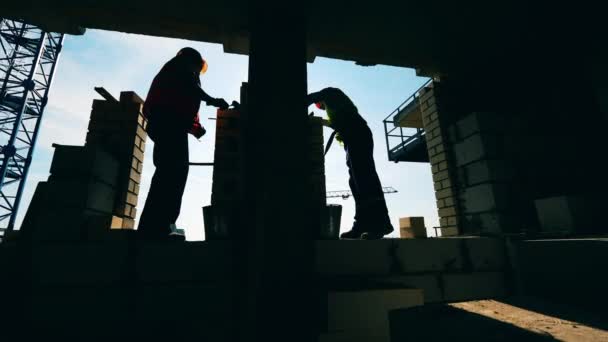 Construtores retroiluminados estão construindo uma parede de edifício — Vídeo de Stock