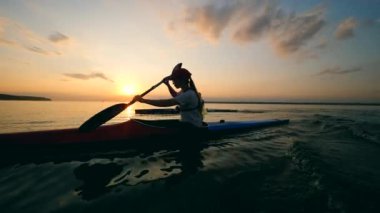 Bir kadın gün batımı gölüboyunca kürek çekiyor.