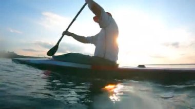 Bir adam yavaş çekimde gölün karşısında kanoyla ilerliyor.