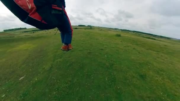 Adam bir yamaç paraşütü uçuruyor, çimenlerin üzerine iniyor.. — Stok video