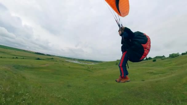 Um atleta voa um parapente sobre o campo verde . — Vídeo de Stock