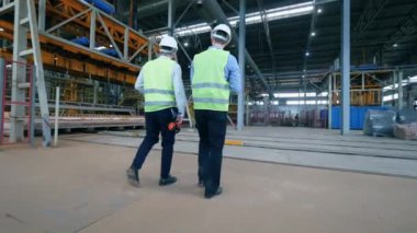 İki erkek mühendis sanayi fabrikasının zemininde yürüyor.