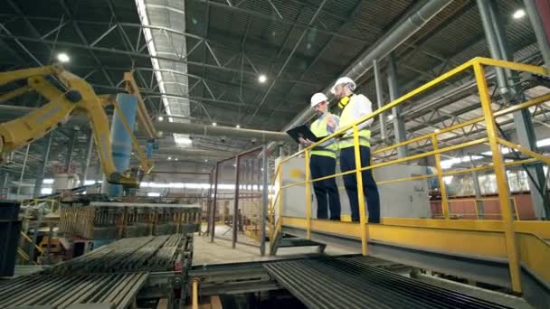 Deux techniciens inspectent un bras robotique dans une usine moderne — Video