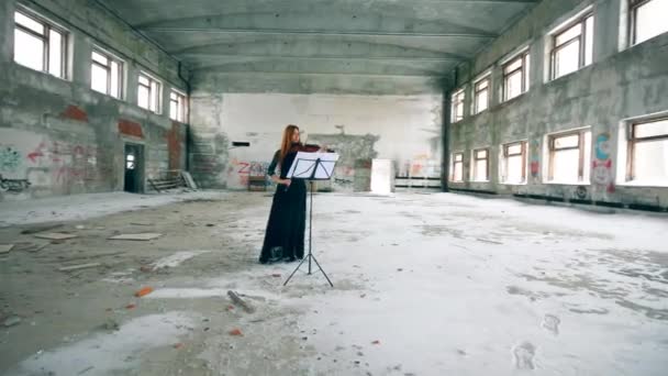 Female fiddler plays violin while standing in abandoned building. — Stock Video