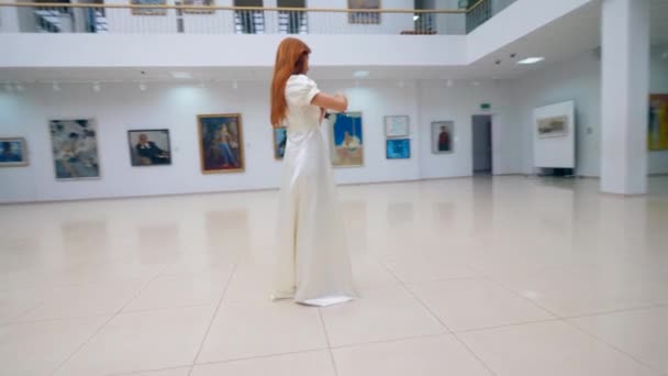 Mujer con un vestido tocando el violín, de pie en una sala del museo . — Vídeos de Stock