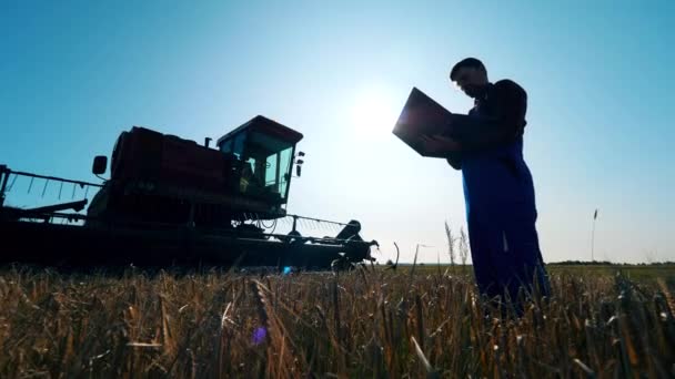 Męski agronom stoi na polu z laptopem i pługiem — Wideo stockowe