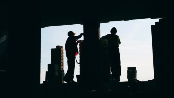 Robotnicy kładą cegły na tle nieba. — Wideo stockowe