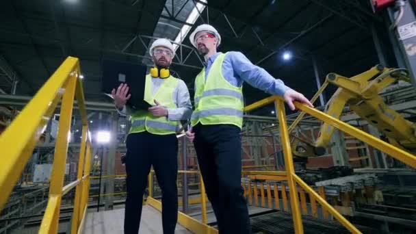 Colleagues stand in a factory facility, checking the work of factory machines. — Stock Video