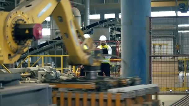 Workers, factory colleagues stand in a facility while a machine works with bricks. — Stock Video