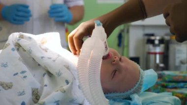 Doktorlar bir çocuğu masadaki bir ameliyata hazırlar, oksijen maskesi verir..
