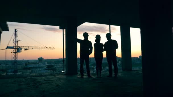 Arquitectos retroiluminados hablando en un edificio en construcción durante la puesta del sol . — Vídeos de Stock