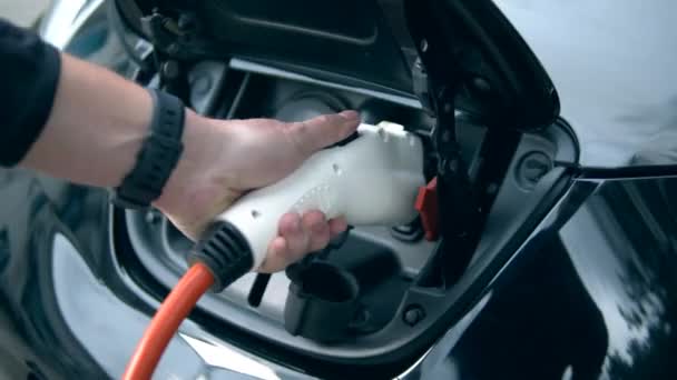 Een man sluit een oplaadkabel aan op zijn elektrische auto. Innovatief elektrisch hybride auto opladen. — Stockvideo