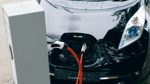케이블이 있는 충전소에 연결된 검은색 자동차. — 비디오