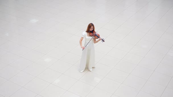 흰색 드레스를 입은 여인이 흰색 타일에 서서 바이올린을 연주하고 있습니다. — 비디오
