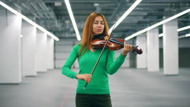 美しい女性は空のホールでバイオリンを弾いています — ストック動画