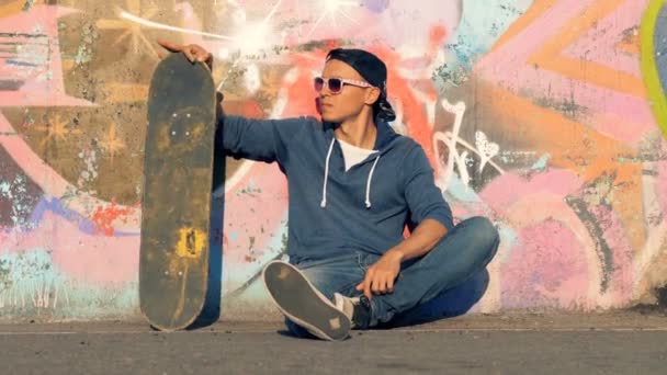 Person sitter med en skateboard. En skridskoåkare sitter på en mark, håller en skateboard. — Stockvideo